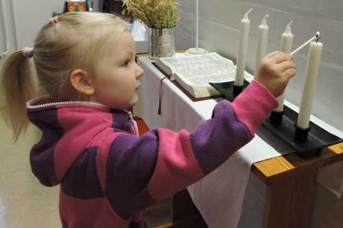 Pieni tyttö sytyttää adventtikynttelikön ensimmäistä kynttilää kerhohuoneen alttarille.