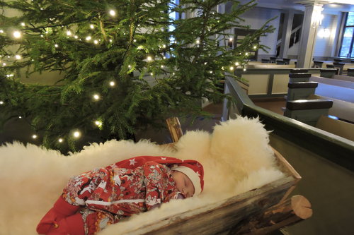Pieni vauva nukkuu kirkossa isossa seimessä joulukuusen vieressä.