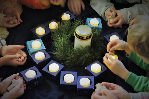 Lapsilla käsissä puuristejä, lapset makoilevat lattialla, jossa kynttilöitä ja hautakynttilä sekä havukrassi.