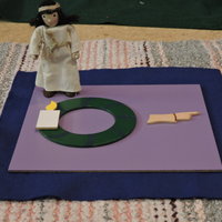 Ensimmäisen adventin ensimmäinen kynttilä vihreän ympyrän päällä, Sormi osoittaa suuntaa. Jeesus -nukke.