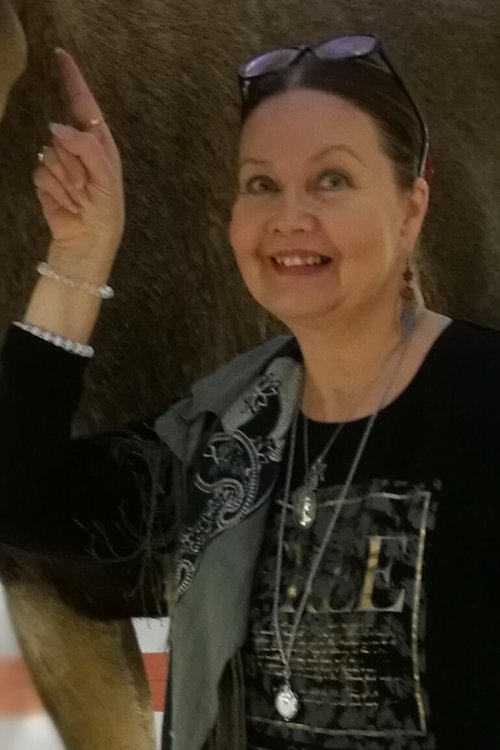 Kuvassa Elina Räsänen hymyilee osoittaen sormellaan ylöspäin.