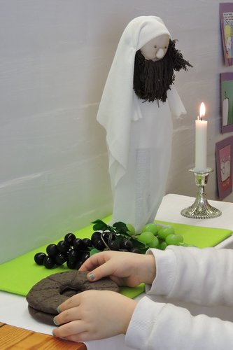 Alttaripöydällä on leipää ja viinirypäleitä sekä Jeesus-nukke ja kynttilä.