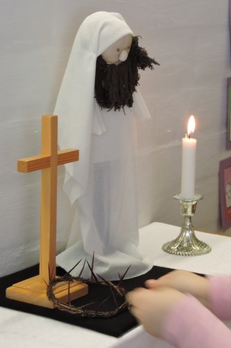 Alttaripöydällä on risti, piikkikruunu, Jeesus-nukke sekä kynttilä.