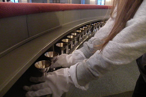 Koululainen asettelee kirkossa pikareita valkoiset puuvillakäsineet kädessä valmiiksi ehtoollista varten.